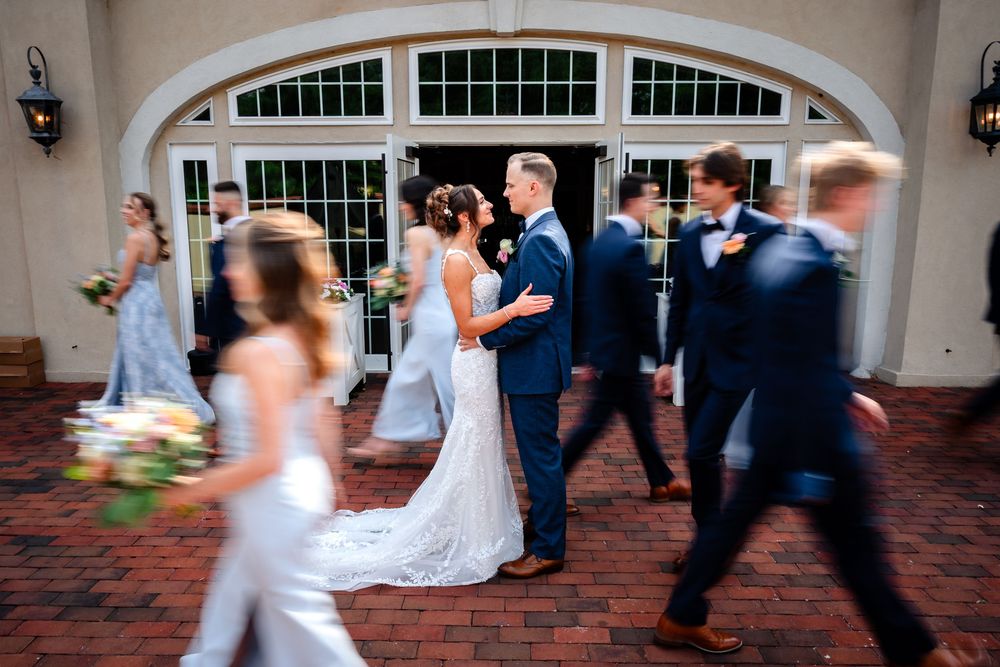 Wedding party dances and celebrates under an elegant arched entrance.