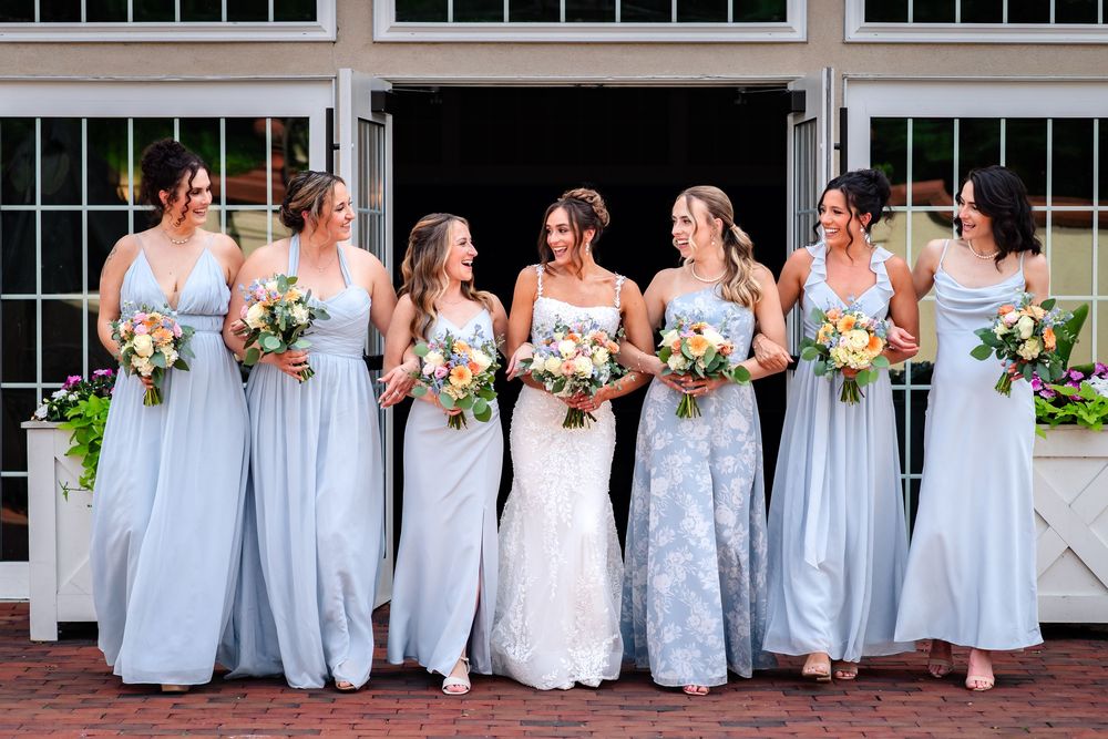 Bridesmaids in light blue dresses pose with bride for outdoor wedding photos.