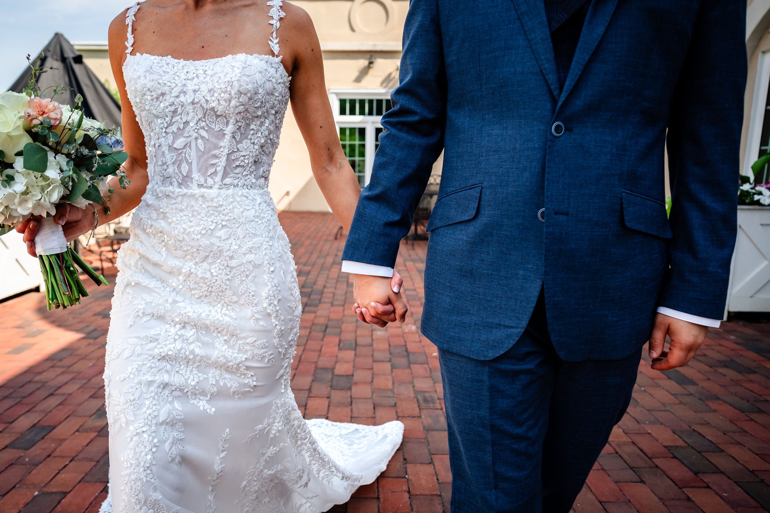 Close-up details of lace wedding dress and navy suit during outdoor ceremony.