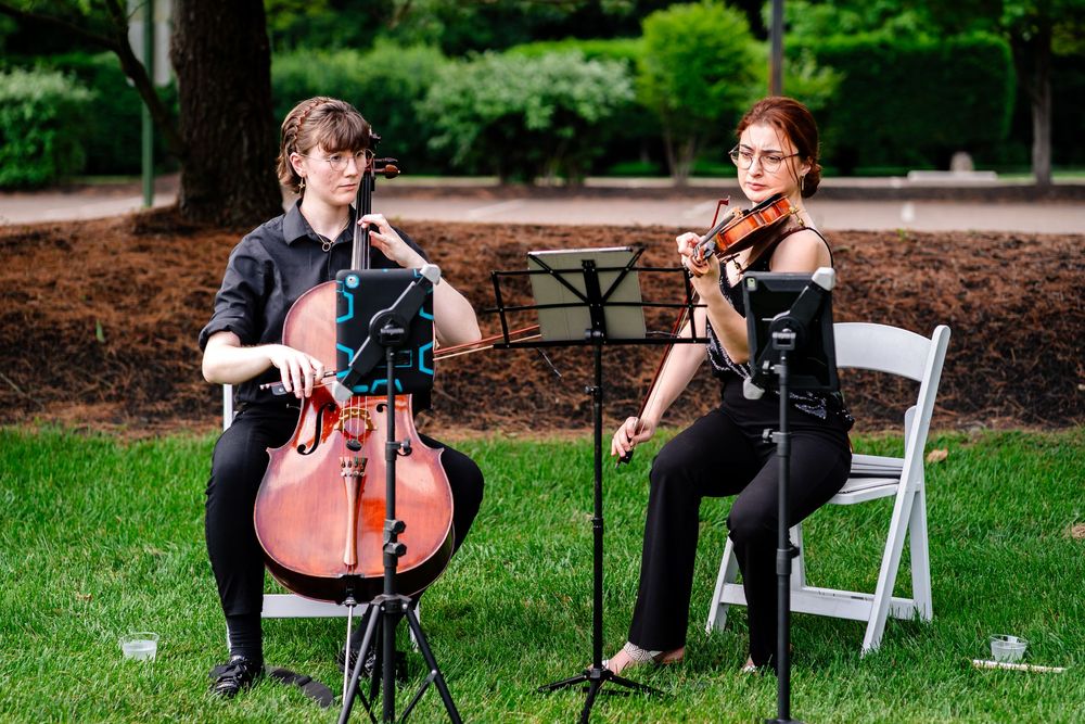 Musicians performing at an outdoor wedding ceremony with white chairs.