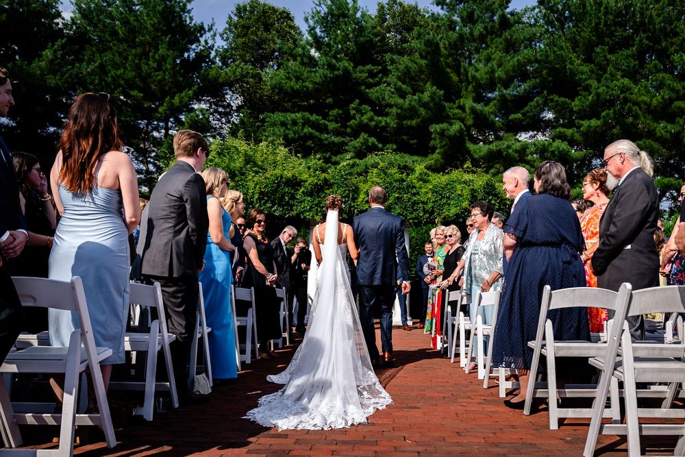 Outdoor wedding ceremony setup with white chairs and guests on a brick pathway.