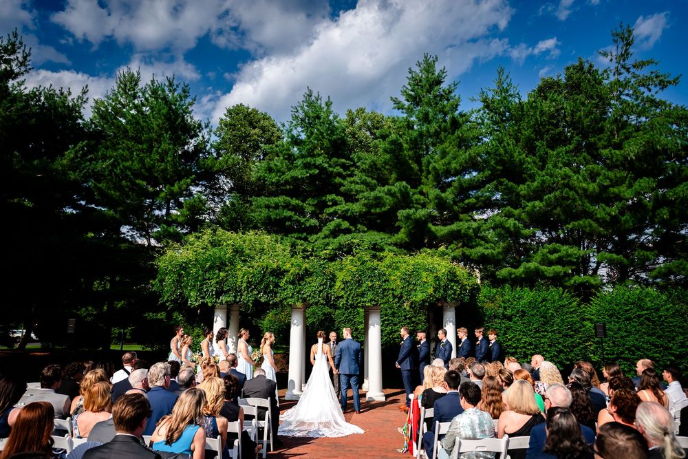 Outdoor wedding ceremony setup with white chairs under bright blue skies and fluffy clouds.