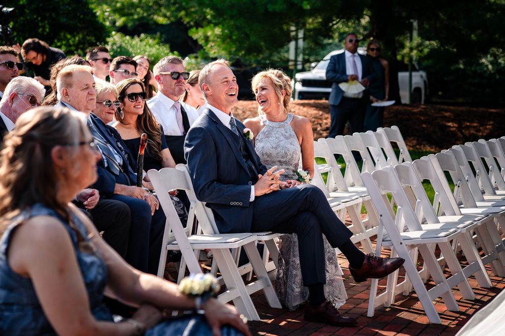 White ceremony chairs arranged in rows on a brick patio for an outdoor wedding.