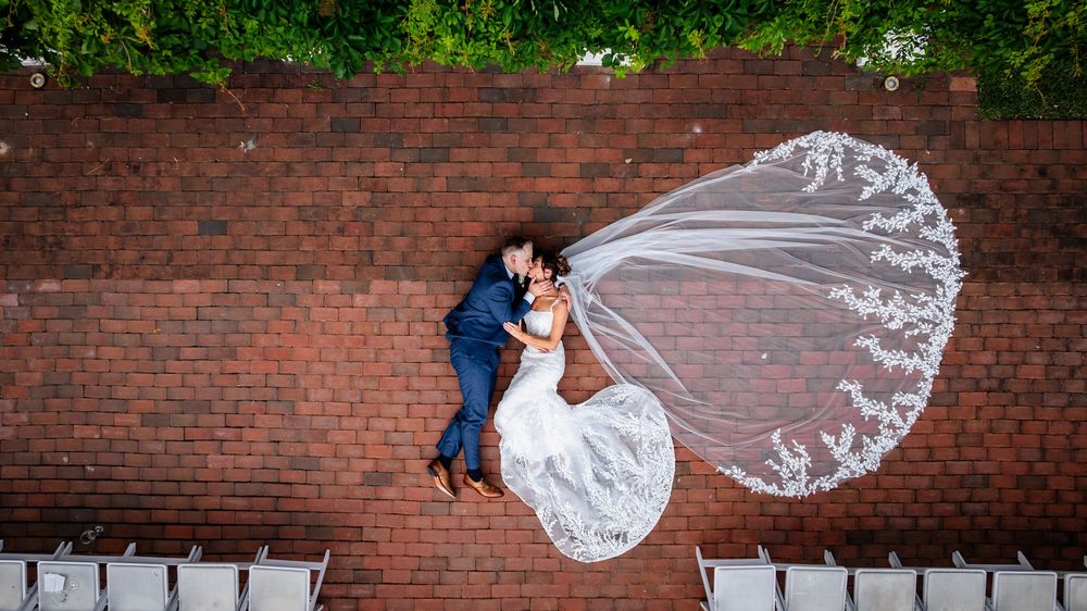 Long flowing bridal veil catches the breeze against a red brick wall backdrop.