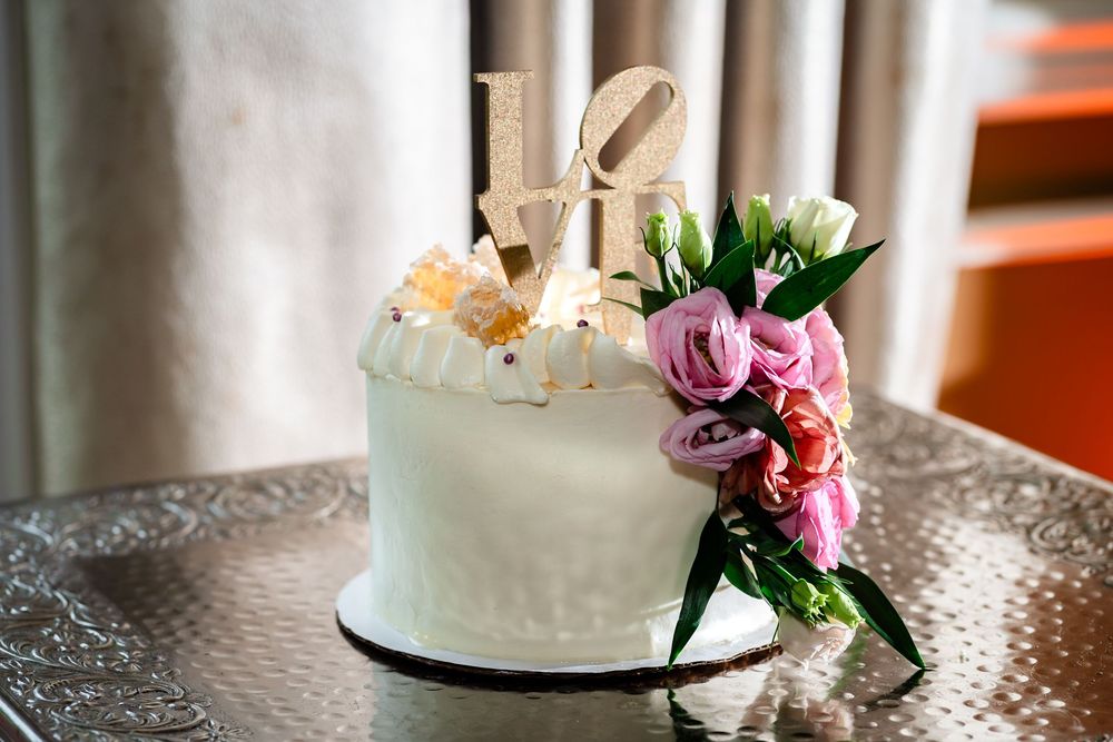 Elegant white wedding cake decorated with fresh flowers sits on a glass table near white columns.