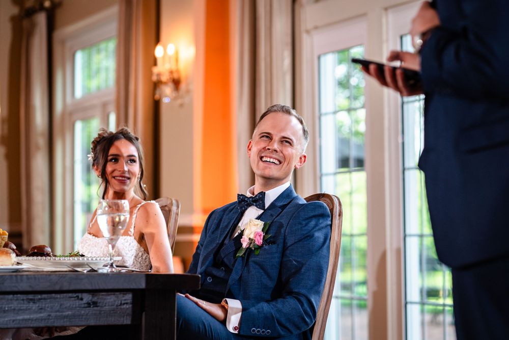Guests laugh and celebrate during emotional wedding speeches at an indoor reception venue.