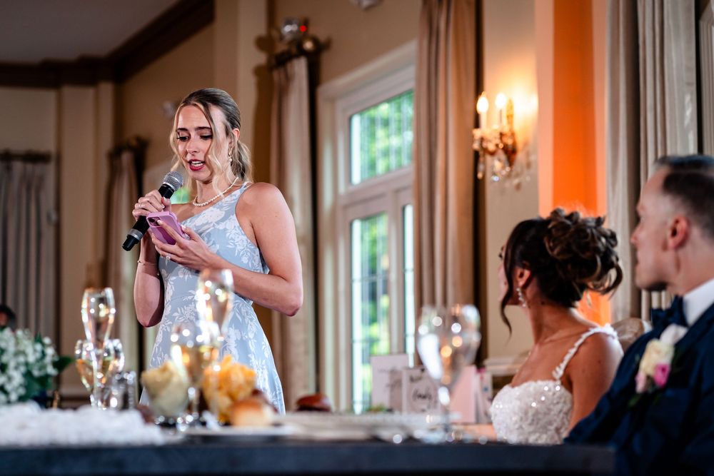 Wedding party members react with laughter during heartfelt reception toasts in an elegant ballroom.