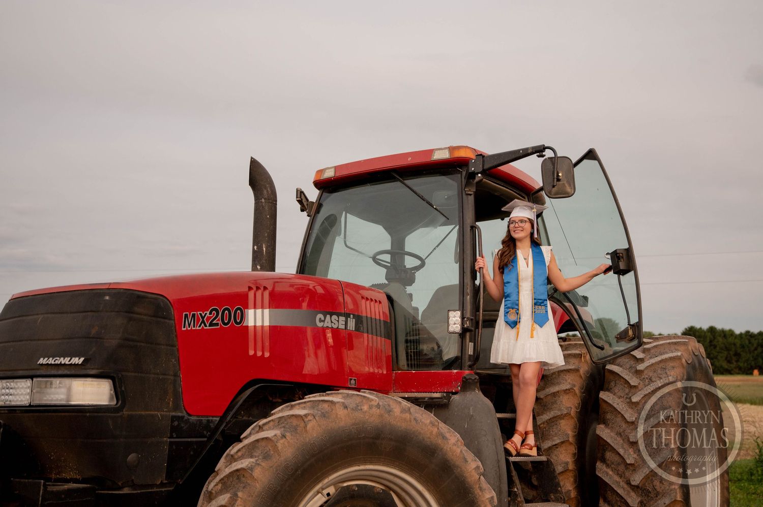 A red Case IH Magnum tractor parked in a field during an overcast day with someone standing on its large wheel.