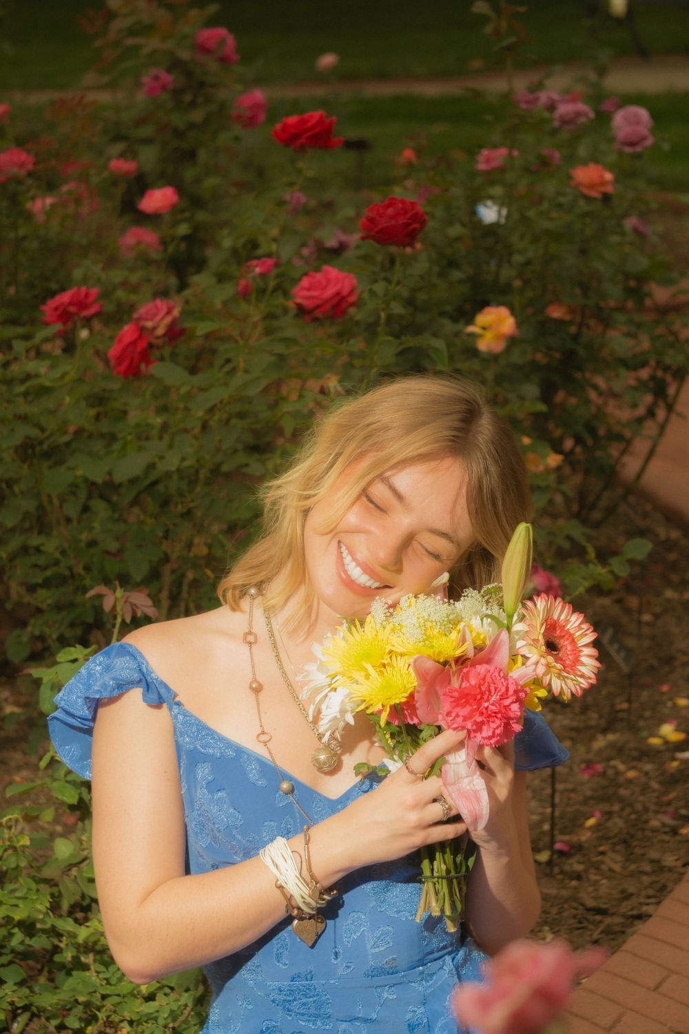 Graduate smells fresh-picked flowers while sitting in a blooming rose garden.