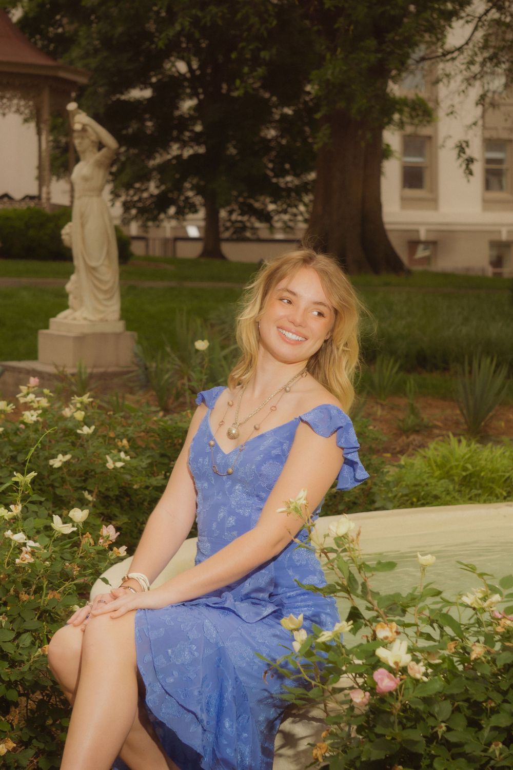 Graduate poses on stone bench surrounded by blooming flowers and greenery.