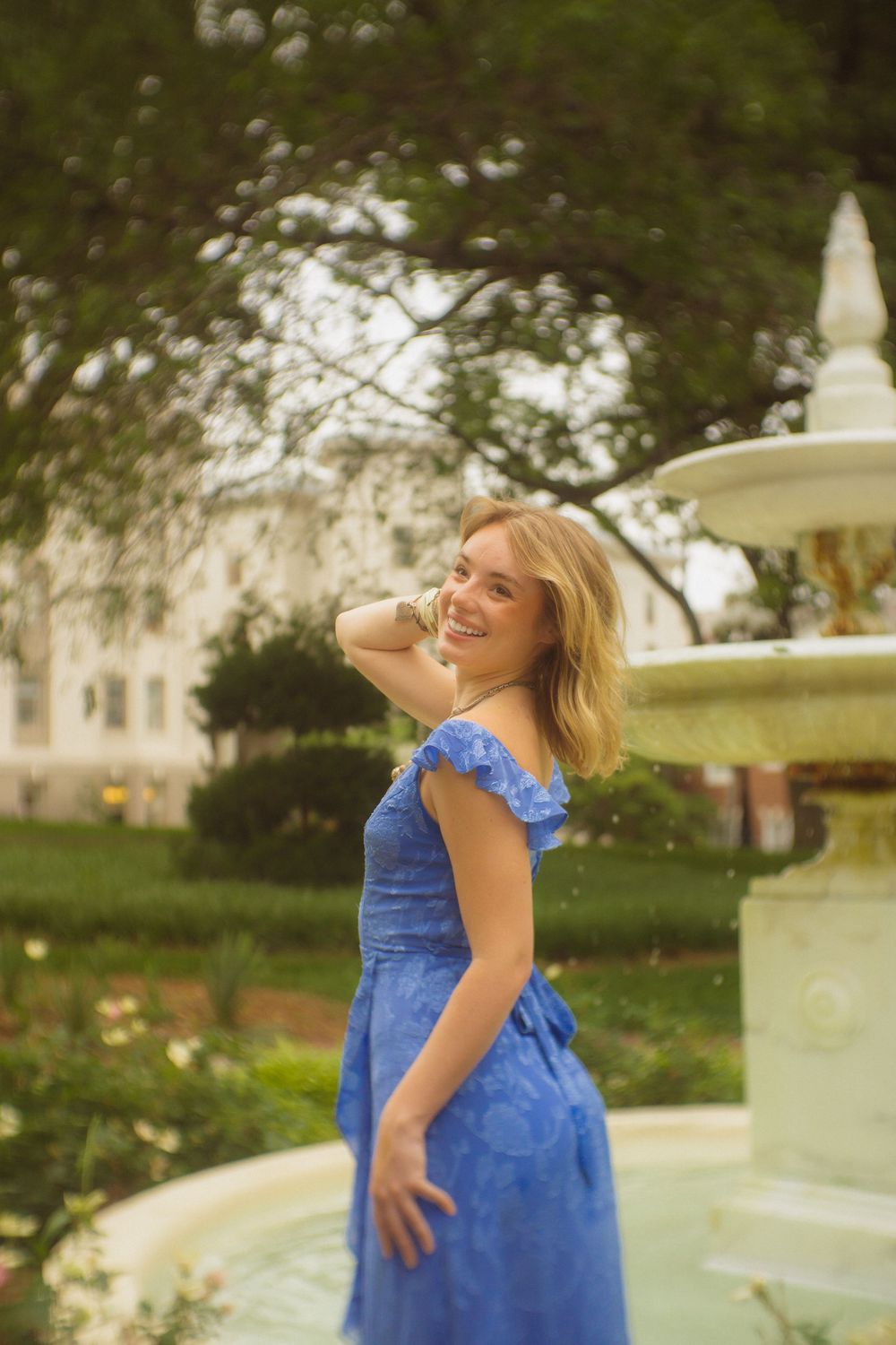 Graduate dances joyfully by fountain during outdoor graduation photo session.