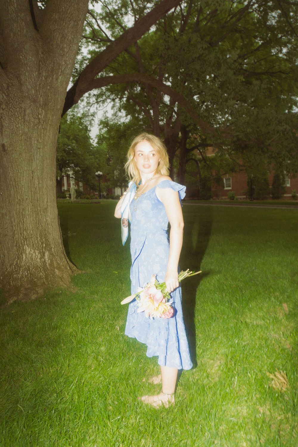 Person in flowing blue dress dances and twirls in a grassy park setting with trees.