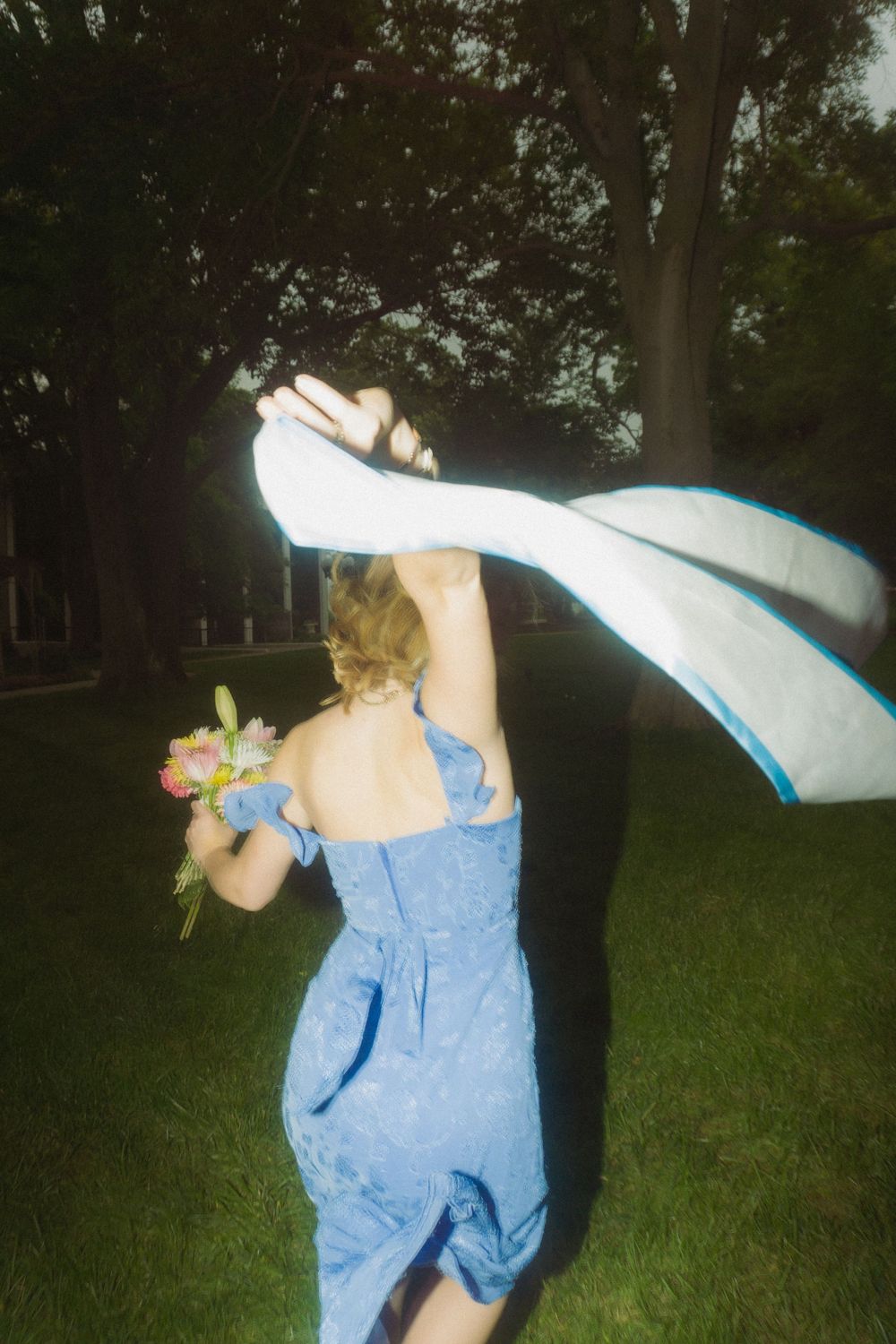 Figure in blue dress creates flowing motion with white fabric against green landscape.