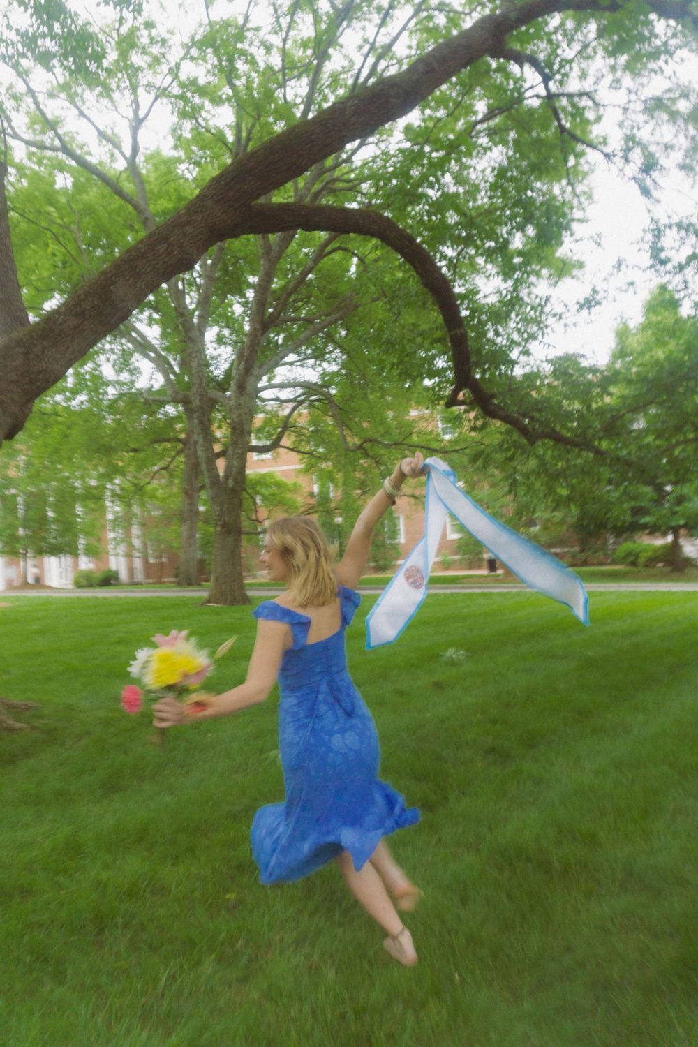 Person in blue dress swings and dances through park setting with trees and grass.
