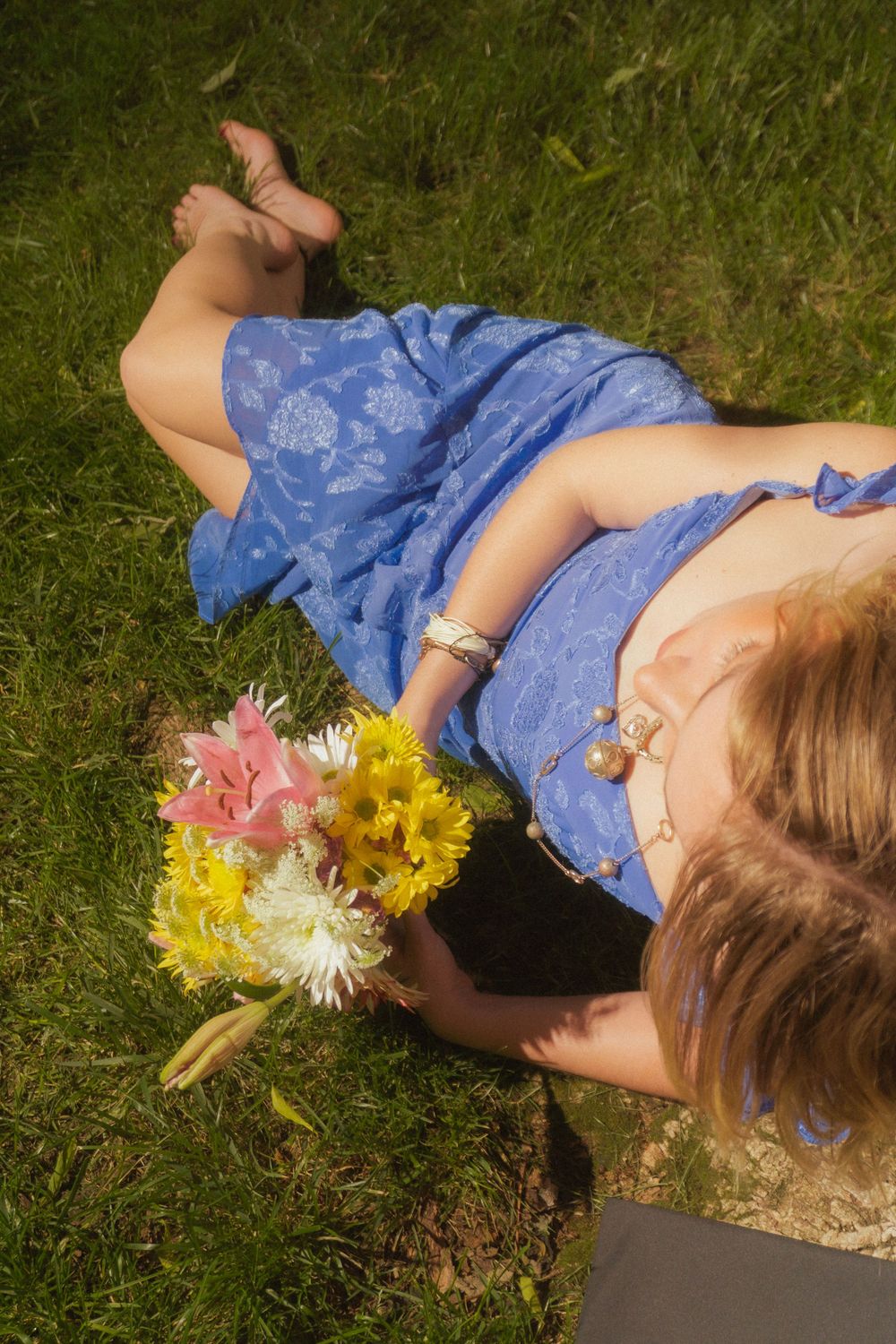 Person lying in grass with colorful flowers in casual graduation photo shoot.