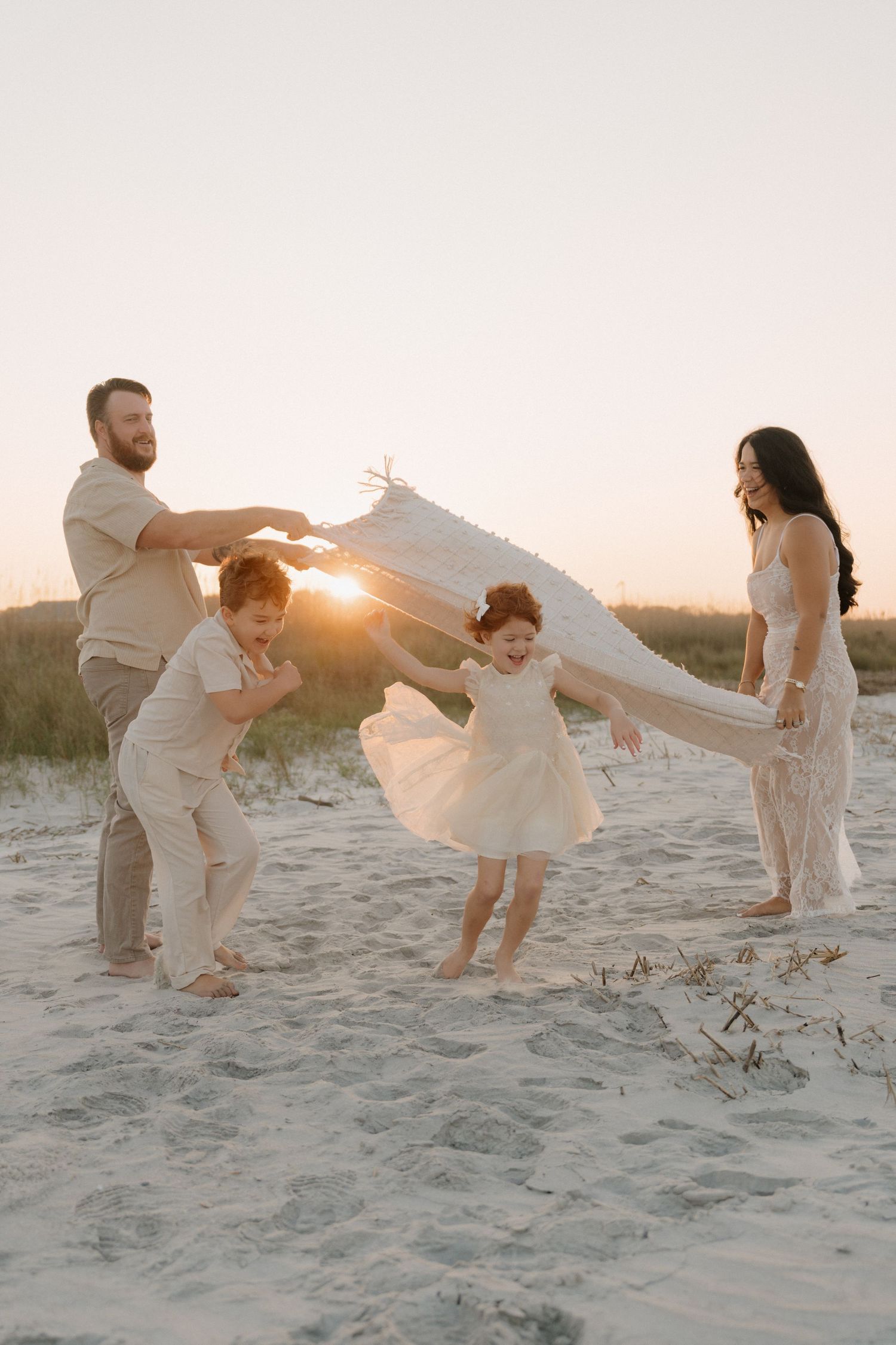 A family stands together in a golden field of tall grass at sunset, children playing in the foreground.