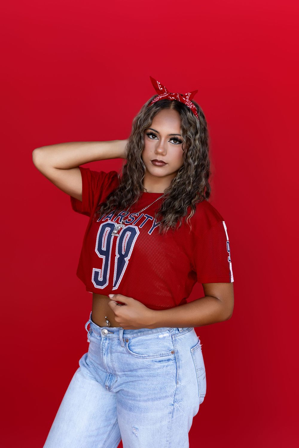 A person in a cropped red t-shirt and light jeans poses against a vibrant red background.