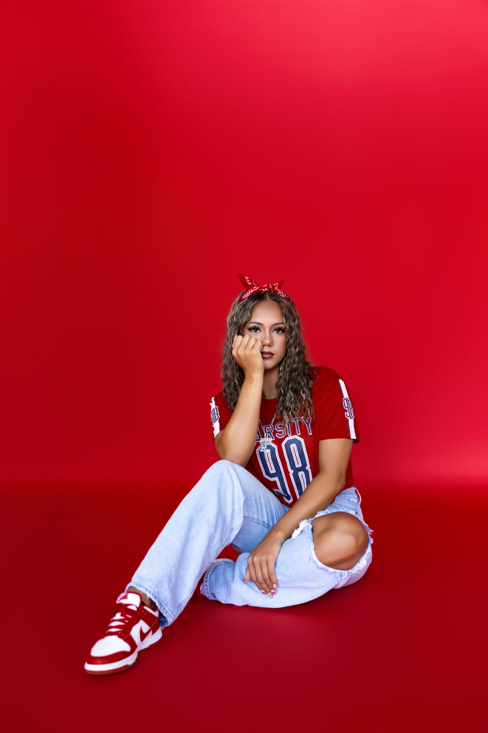 A model in casual attire with Nike shoes poses artistically against a vibrant red studio background.