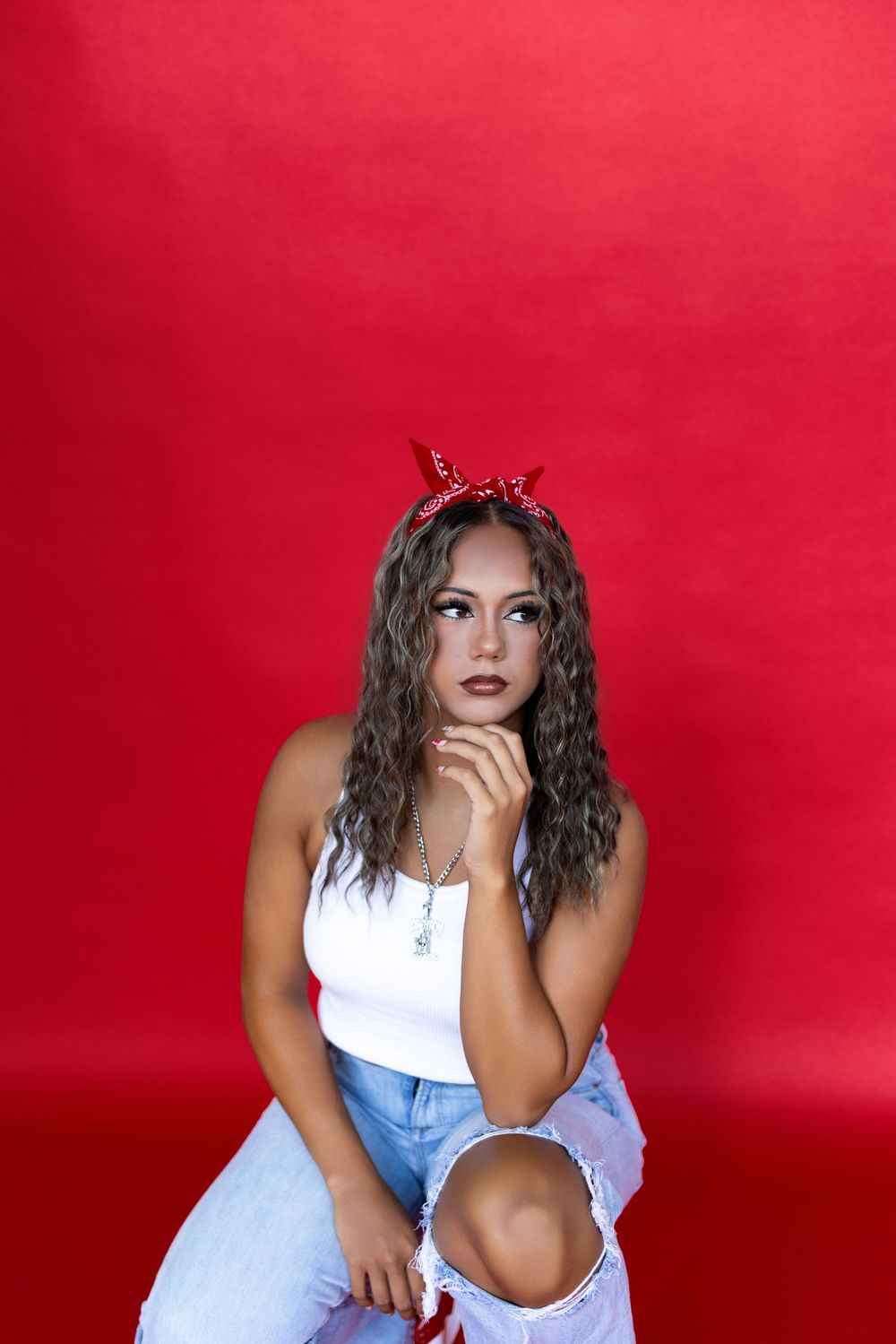 Fashion model in white top and denim poses against vibrant red backdrop in a dynamic photoshoot series.