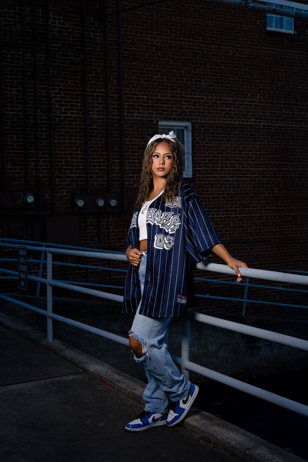 Athlete in pinstriped baseball uniform poses against brick wall background in moody lighting at dusk.
