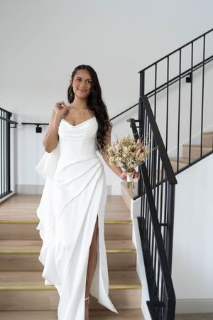 A person in a flowing white dress poses playfully in a bright interior space with black railings.