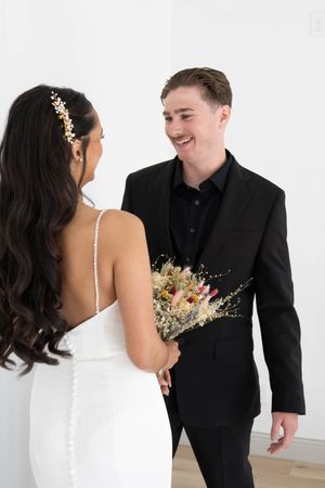 A couple in wedding attire share an intimate moment against a white backdrop.