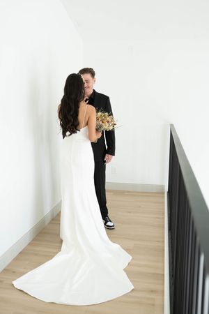 A bride and groom pose together in an elegant white room with wooden floors.