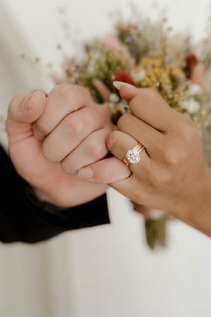Close-up shots of intertwined hands with an engagement ring and dried flower bouquet.