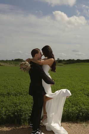 Romantic wedding photoshoot in a sunny field with dramatic sky and natural backdrop.