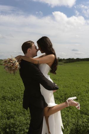 Sun-lit wedding photos showing tender moments between newlyweds in a green field.