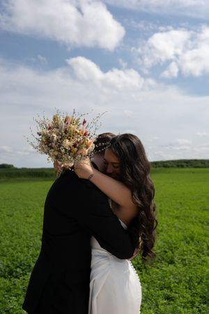 A wedding couple sharing a tender moment in a green field under blue summer skies.