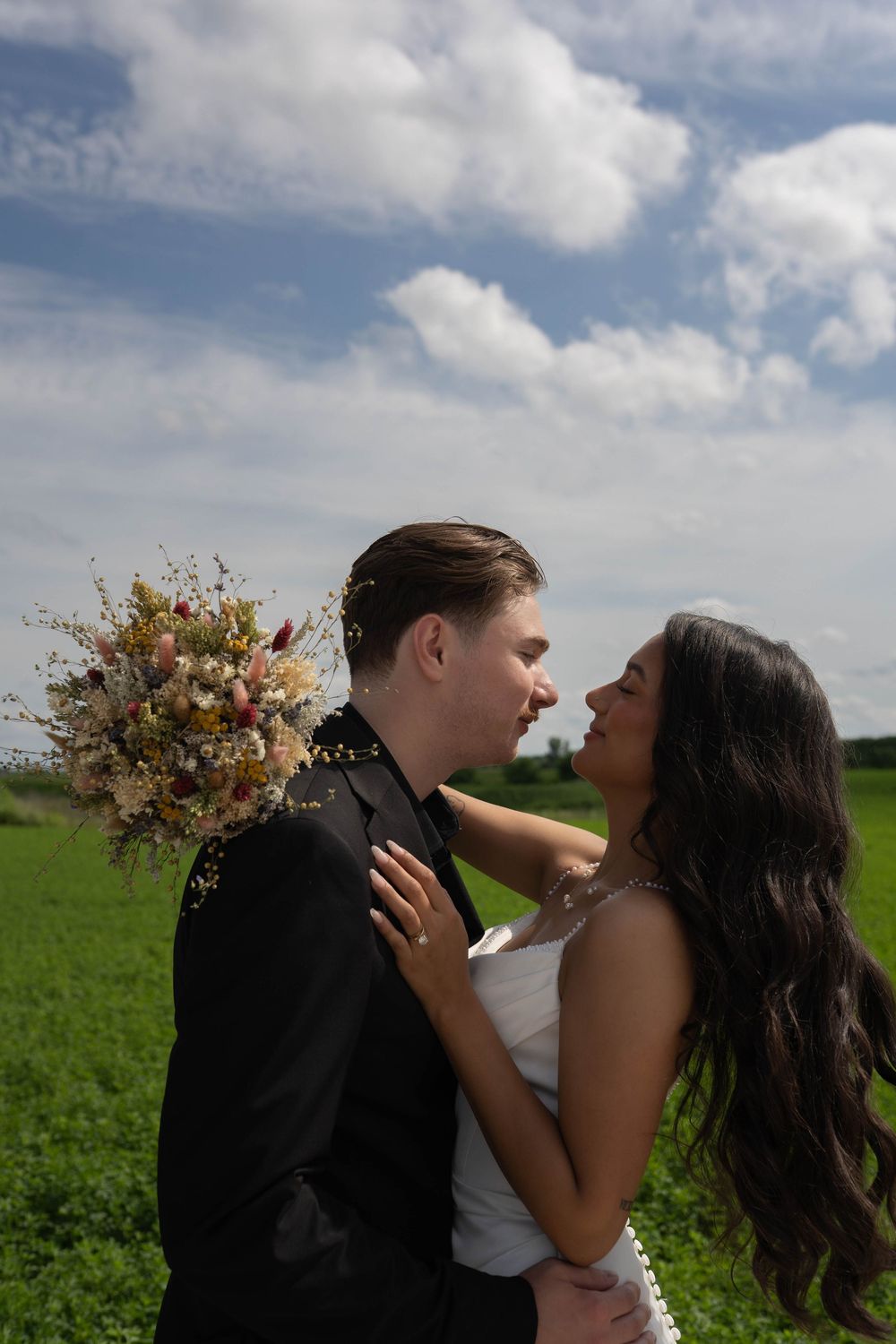 Intimate wedding moment captured in a lush green field under cloud-filled sky.
