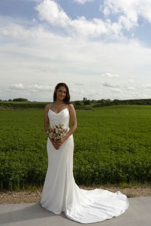 A beautiful bridal portrait showcasing a white wedding dress with train against vibrant green farmland.