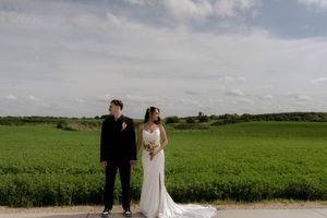 A wide-angle wedding photo showing a couple standing together in expansive green farmland.
