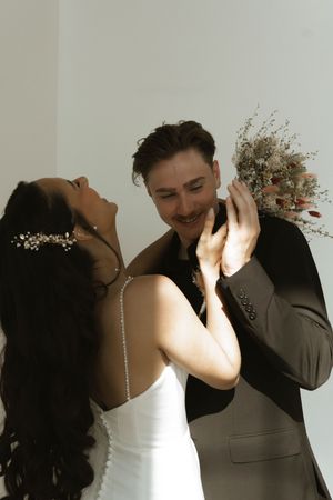 A joyful moment between a couple in wedding attire sharing laughter against a light background.