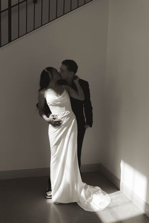 A romantic black and white portrait of newlyweds embracing near a staircase.