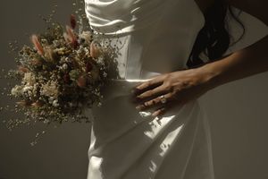 Close-up detail of a wedding dress and dried flower bouquet in dramatic lighting.