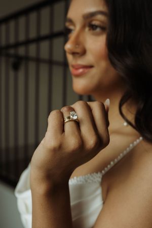 Close-up of an elegant engagement ring being showcased on a hand with a pearl necklace in the background.
