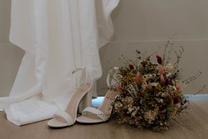 White bridal shoes and dried flower bouquet against white fabric backdrop.