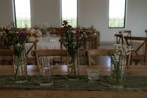 Rustic wedding reception setup with floral centerpieces and wooden chairs in natural light.