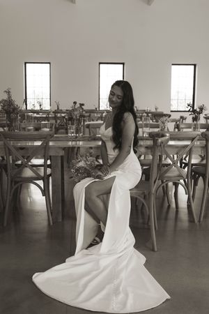 Bride in white dress poses gracefully near wooden reception tables.