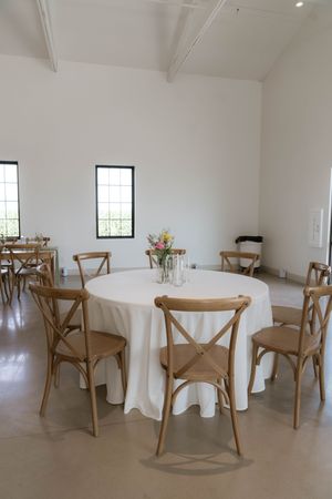 Minimalist reception venue with wooden cross-back chairs and round tables.