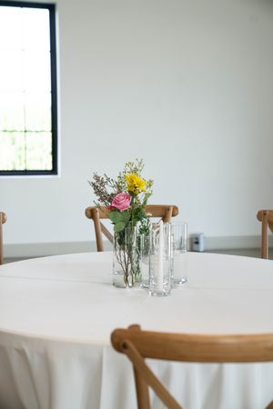 Round tables with white tablecloths and rustic wooden chairs in bright venue.