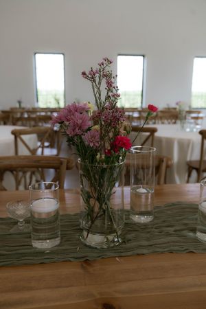 Pink and red floral centerpiece in glass vase on wooden table with green runner and tea lights.