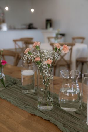 Delicate pink carnations and baby's breath in glass vase on rustic wooden table with sage runner.