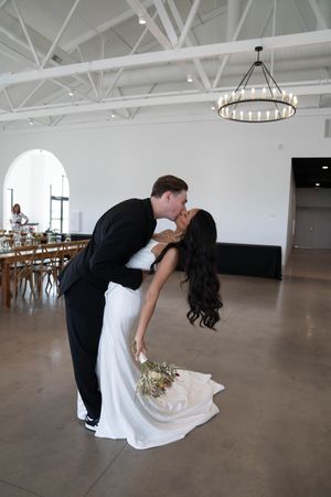 Wedding couple performs dramatic dance dip in bright indoor venue.