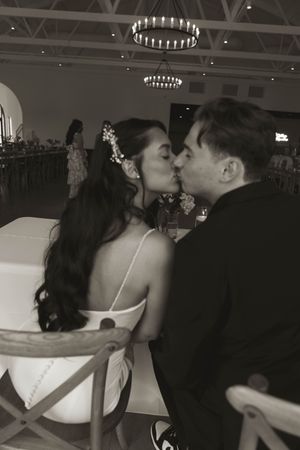 A couple shares a kiss at their wedding reception under elegant circular chandeliers.