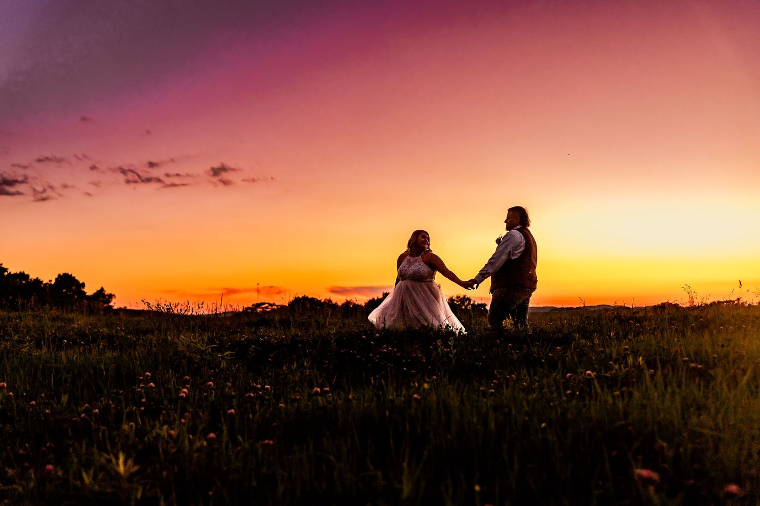 newlyweds walk in field at sunset