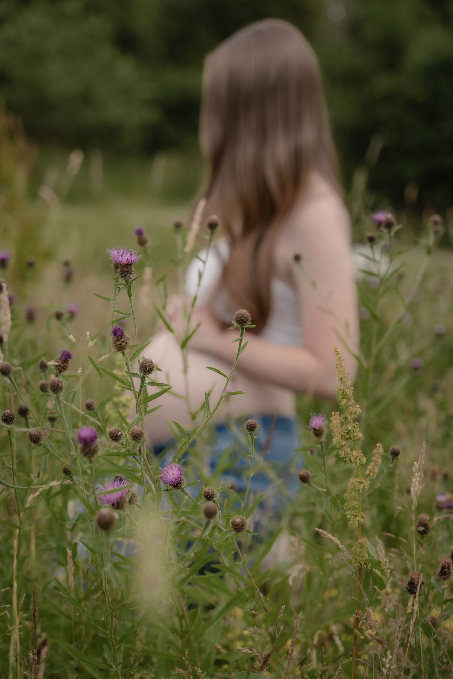 A close-up of a pregnant woman’s belly, gently cradled by her hand, surrounded by tall purple wildflowers in a peaceful outdoor field — a qu