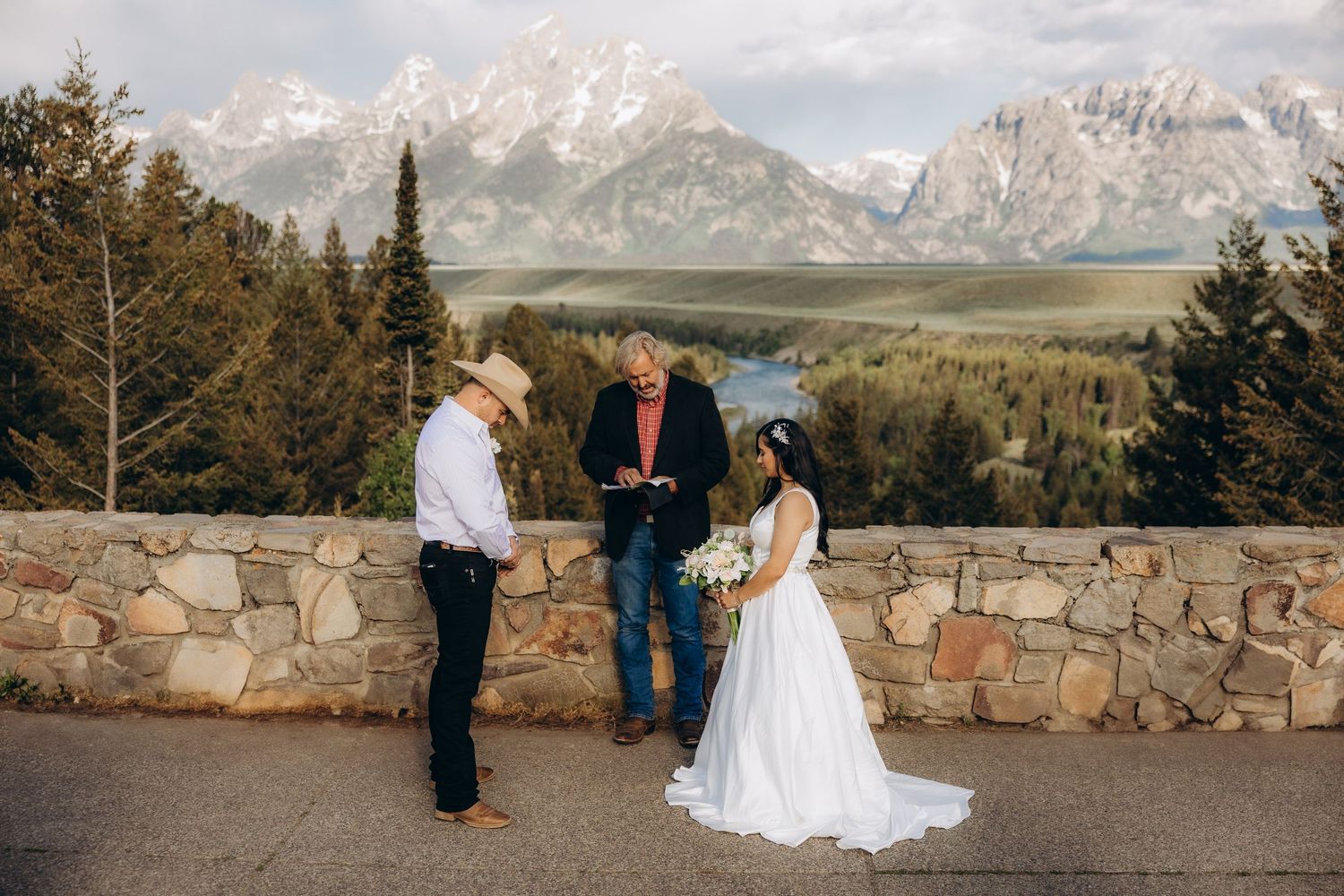 A scenic outdoor ceremony takes place at a stone observation point overlooking majestic mountain peaks in Grand Teton National Park.
